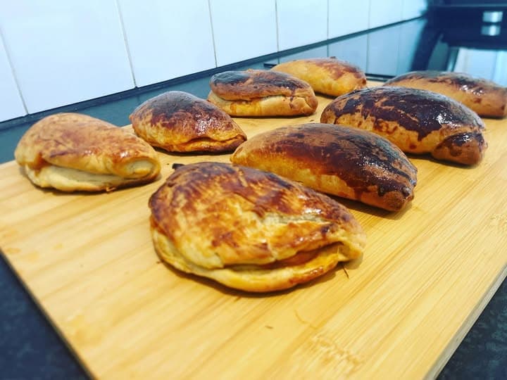 Golden-brown crescent-shaped pastries with a shiny crust on a light wooden cutting board.
