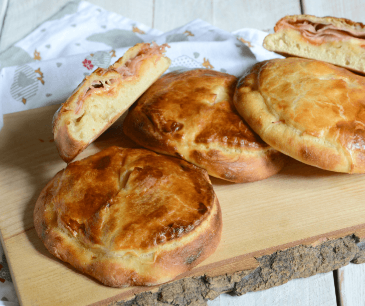 Golden-brown round pastries filled with ham and cheese on a rustic wooden cutting board.