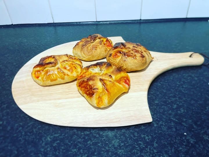 Four golden-brown savory pastries with visible filling on a wooden pizza peel board.