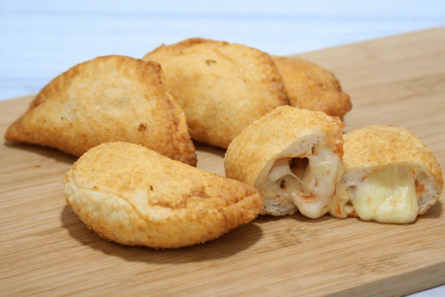 Crispy golden fried pastries on a wooden board, one halved to show melted cheese.